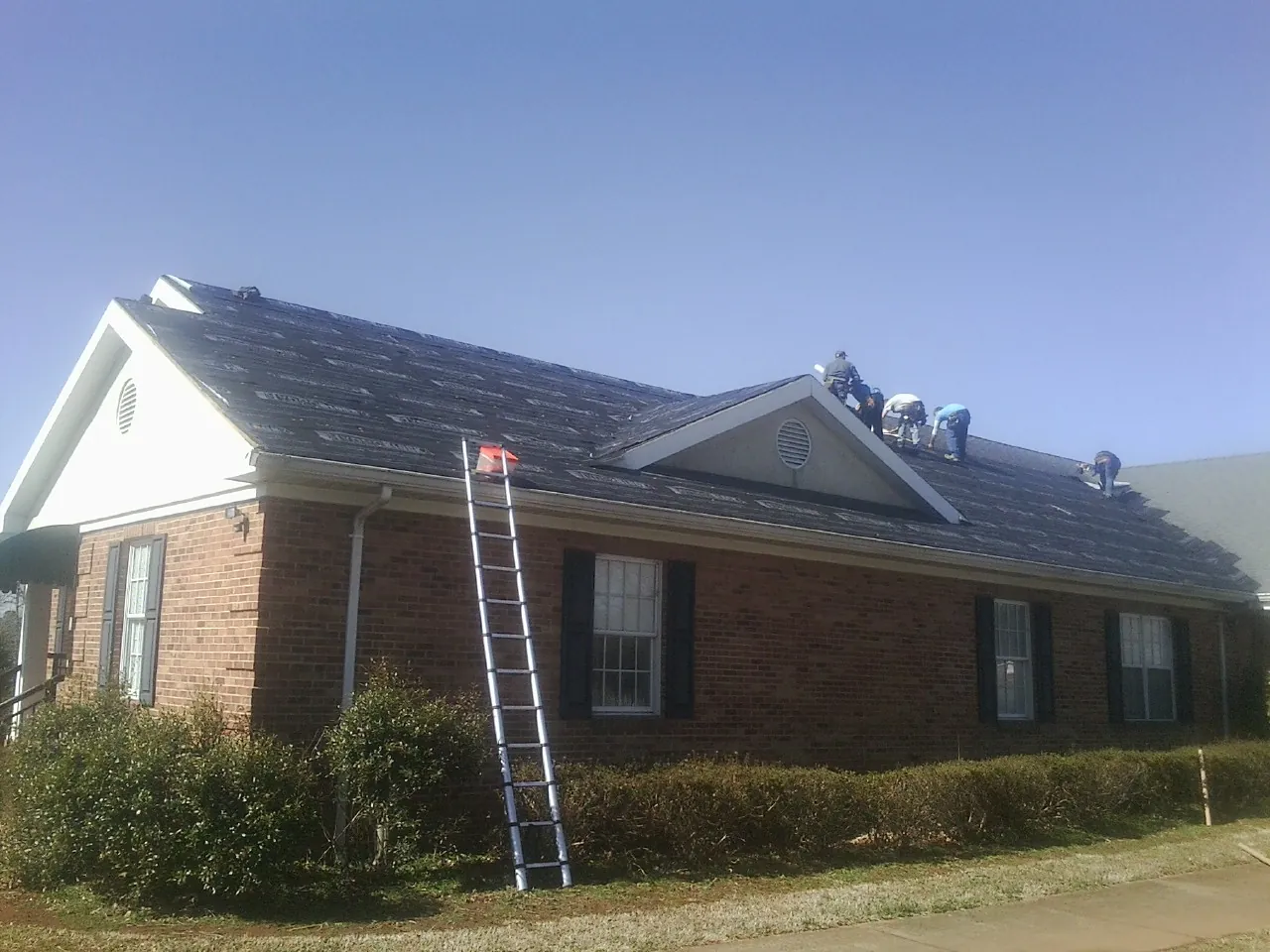 Crew tearing shingles off a brick ranch roof with a ladder set — Emergency Roof Repair work by our crew in Moline