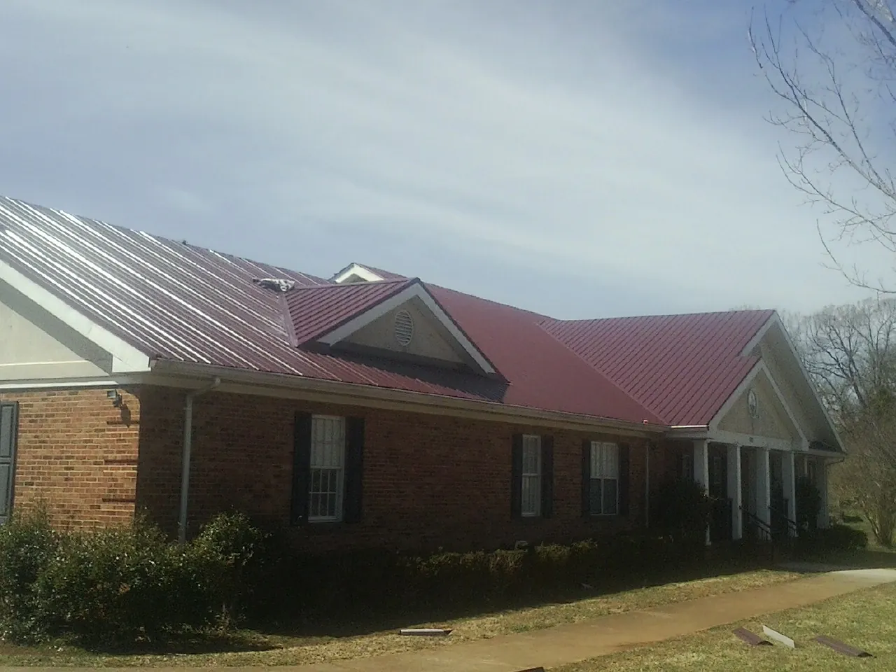 Red metal roof with gabled entries on a long brick building, from a Hail Damage Roof Repair job in Moline