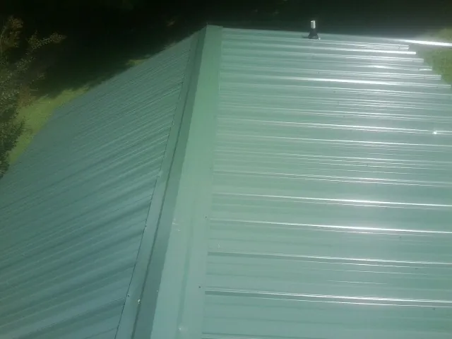 New green metal panels meeting at the ridge of a roof — Flat Roof Repair work by our crew in Moline