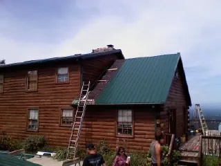 Green metal roof going on a two story log home with ladders set in Moline