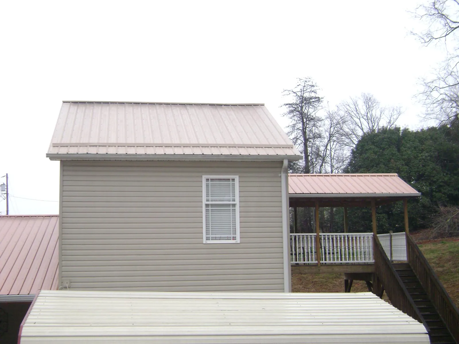 Tan metal roofs on a two story addition and attached porch, from a Roof Replacement job in Moline